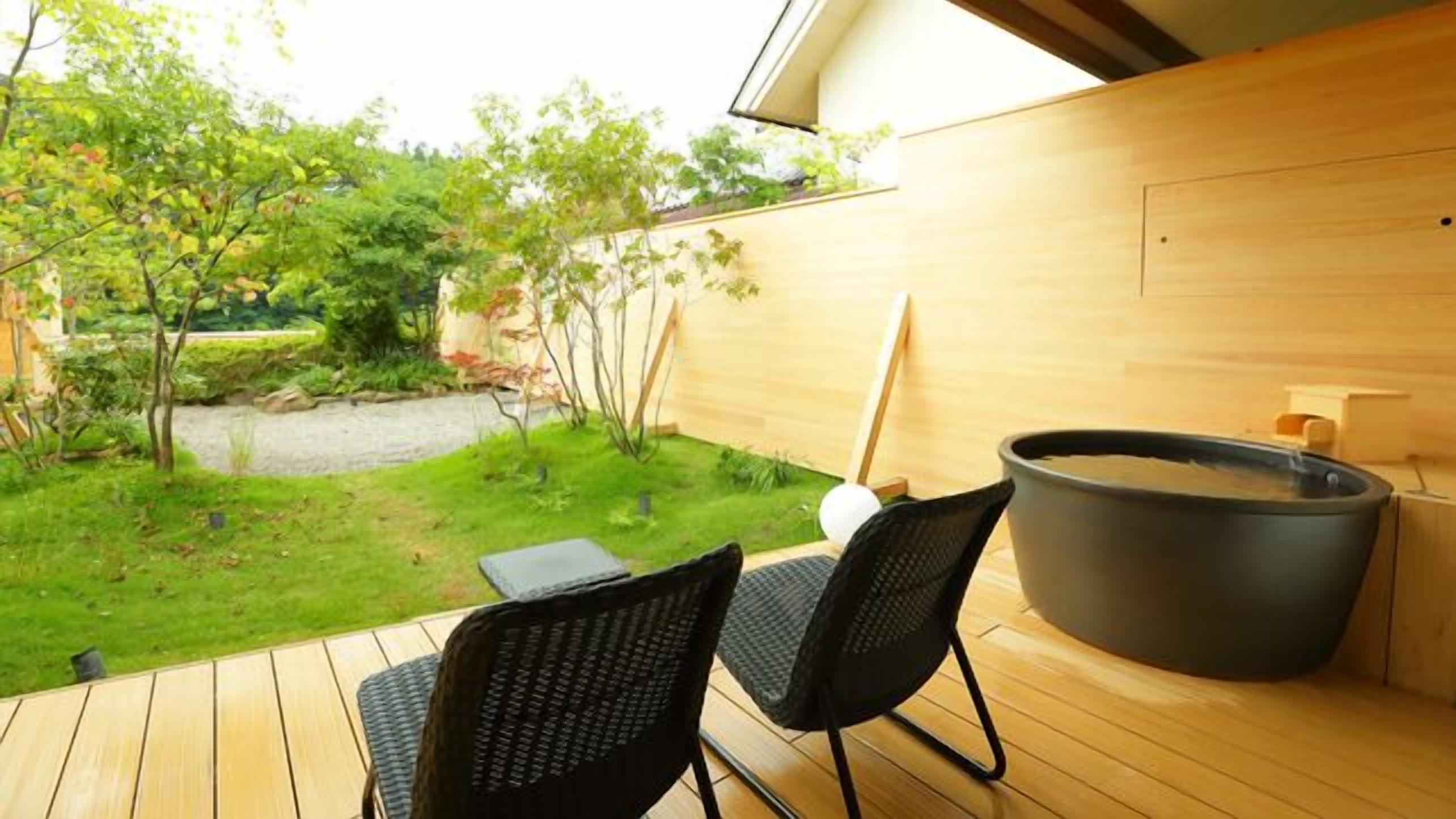 A wooden deck with two chairs, a hot tub, and a view of a garden.