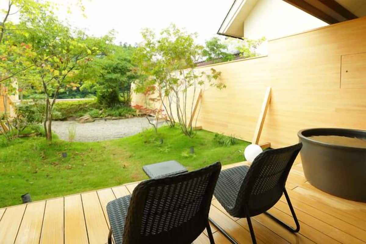 A wooden deck with two chairs, a hot tub, and a view of a garden.