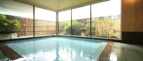 An indoor swimming pool with clear glass walls, a tiled floor, and a wooden ceiling.