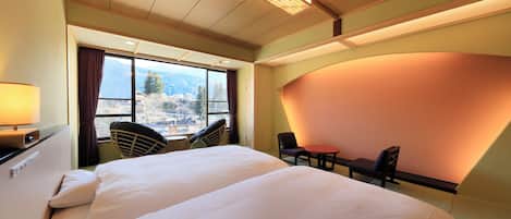 Habitación de hotel con una cama grande, un escritorio, una silla y vistas a las montañas a través del ventanal.