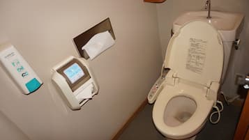 Et badeværelse med toilet, papirhåndklædeholder og sæbedispenser.