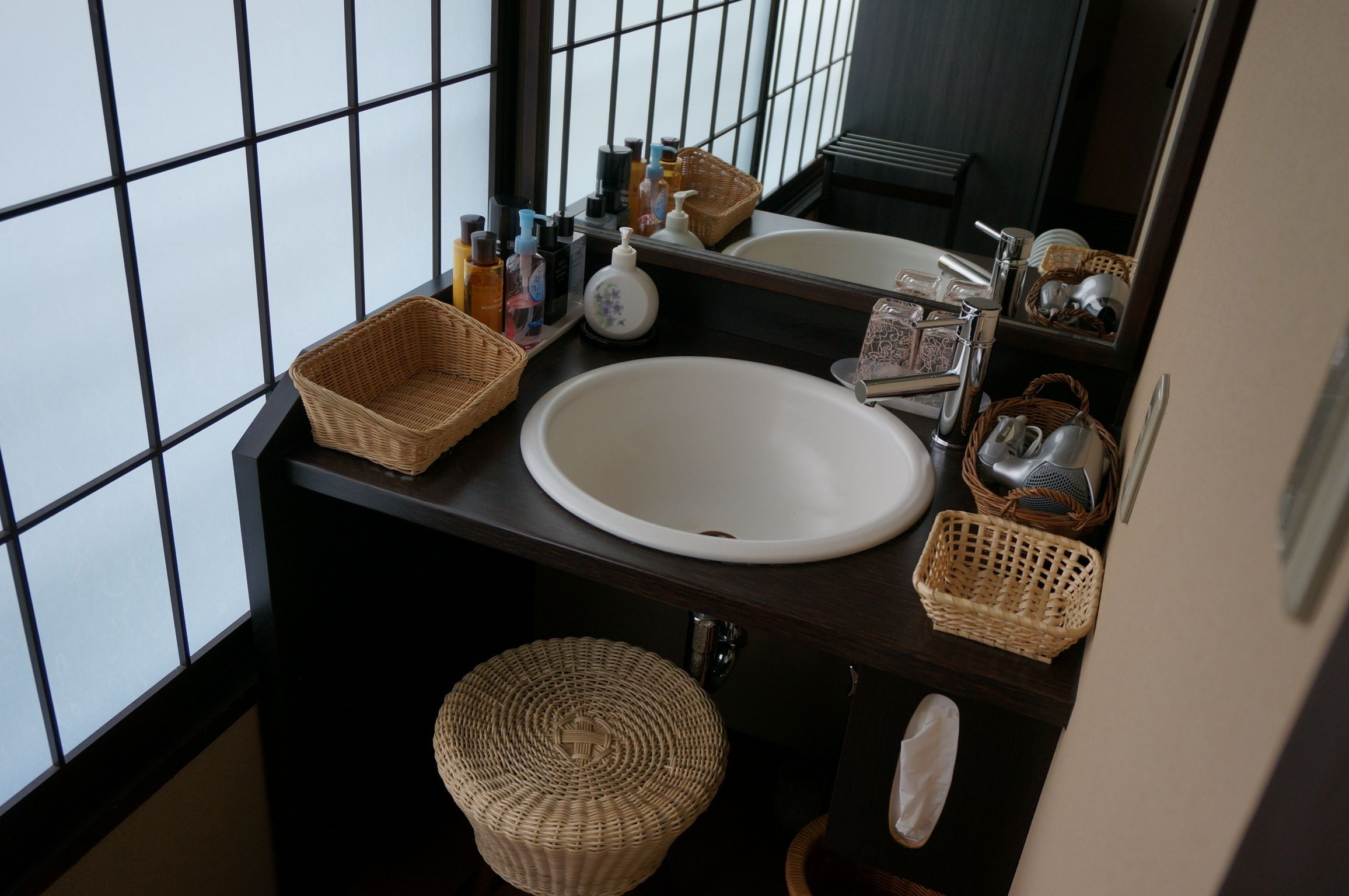 A bathroom with a large window, a white sink, and wicker baskets.