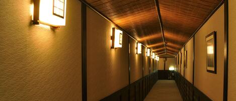 A corridor with wooden ceiling and walls, illuminated by wall-mounted lights.