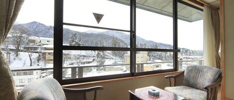 A room with two chairs and a table, large windows with a view of snow-covered mountains and buildings.
