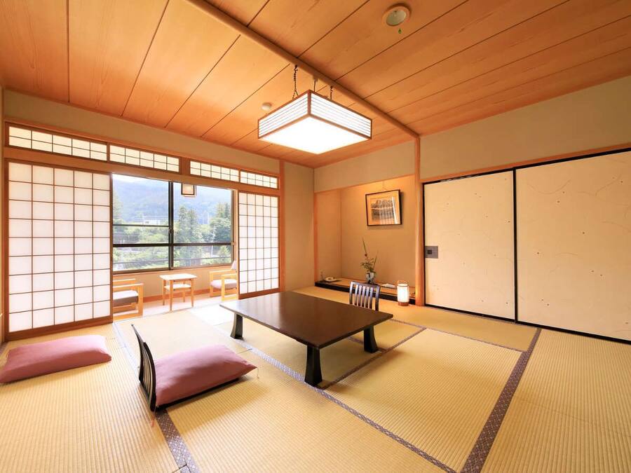 Een traditionele Japanse kamer met tatami vloeren, een lage tafel, schuifdeuren en uitzicht door de ramen.