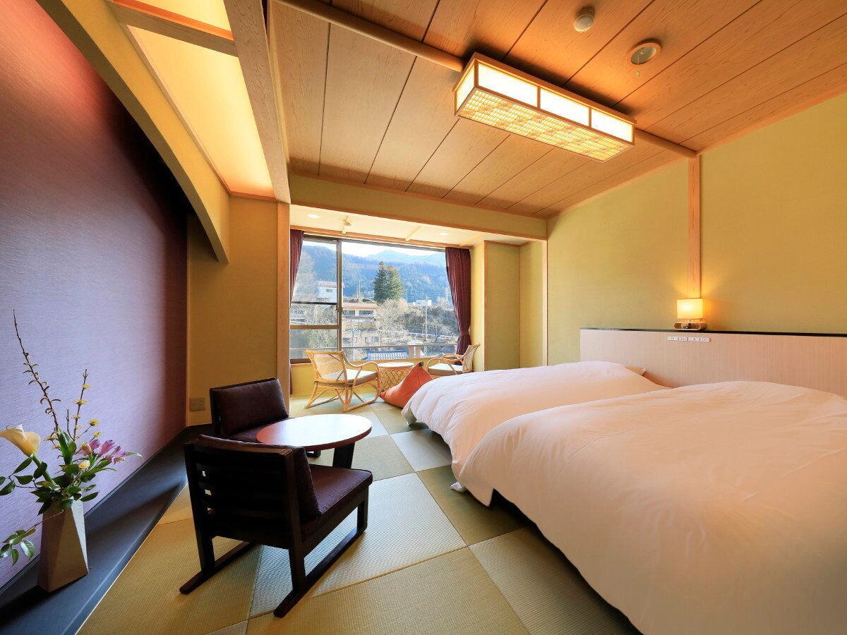 A hotel room with a bed, a chair, a small table, and a view of the outdoors.