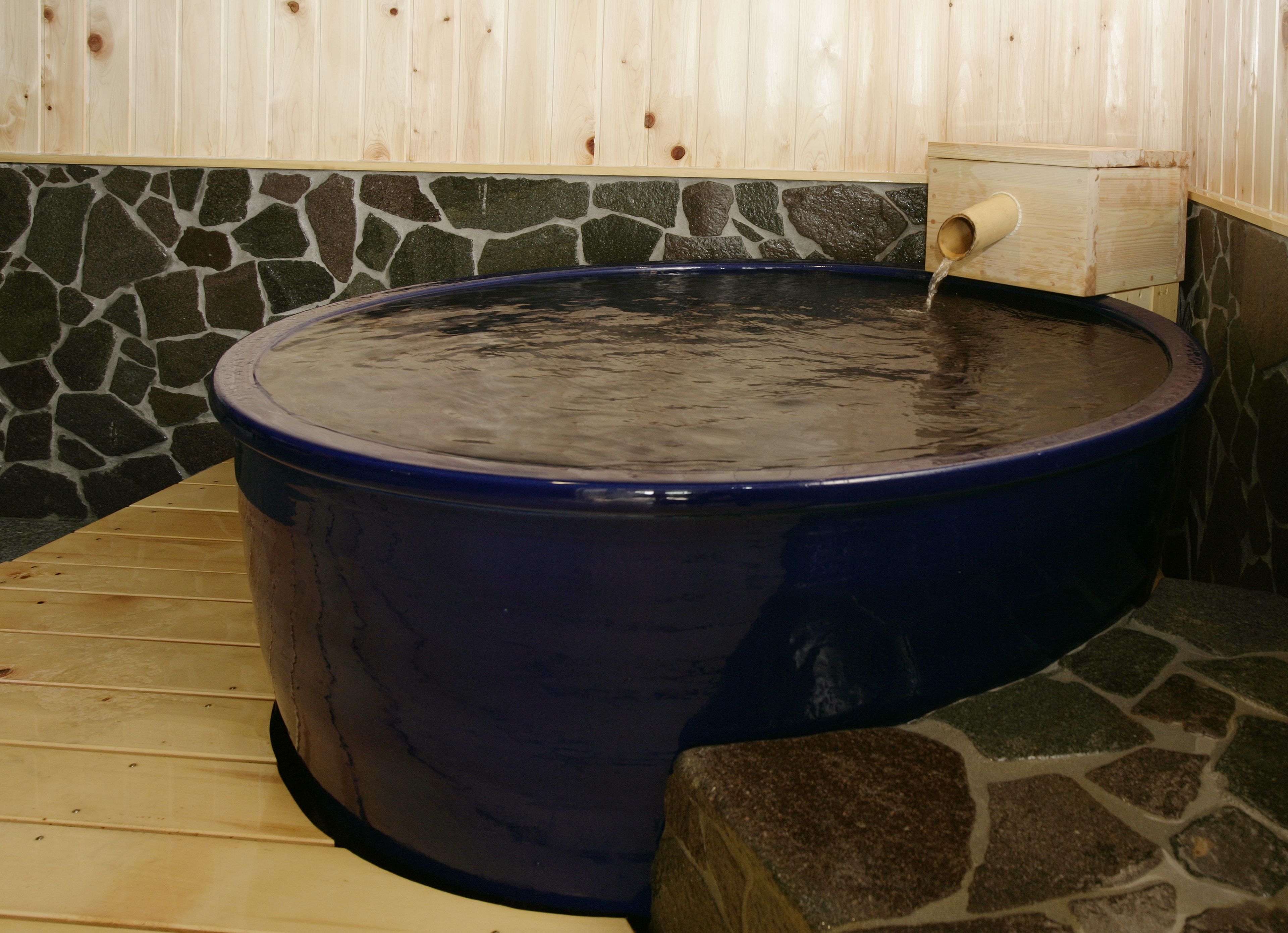 Un bain à remous revêtu de pierres, avec un banc en bois et un mur en bois bordé de pierres.