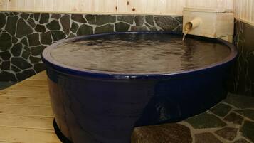 Un bain à remous revêtu de pierres, avec un banc en bois et un mur en bois bordé de pierres.