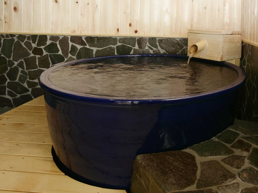 Un bain à remous revêtu de pierres, avec un banc en bois et un mur en bois bordé de pierres.