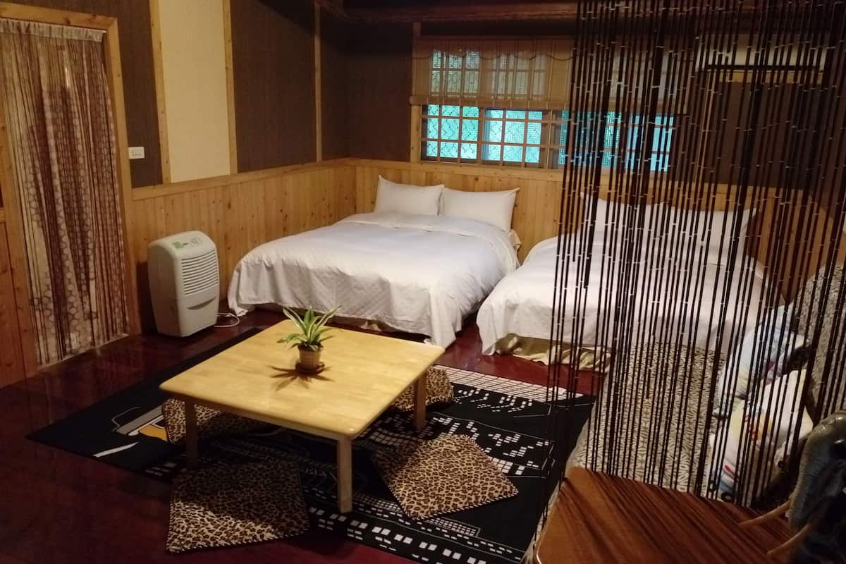 A traditional Japanese-style room with two beds, a small table with a plant, and a window with bamboo blinds.