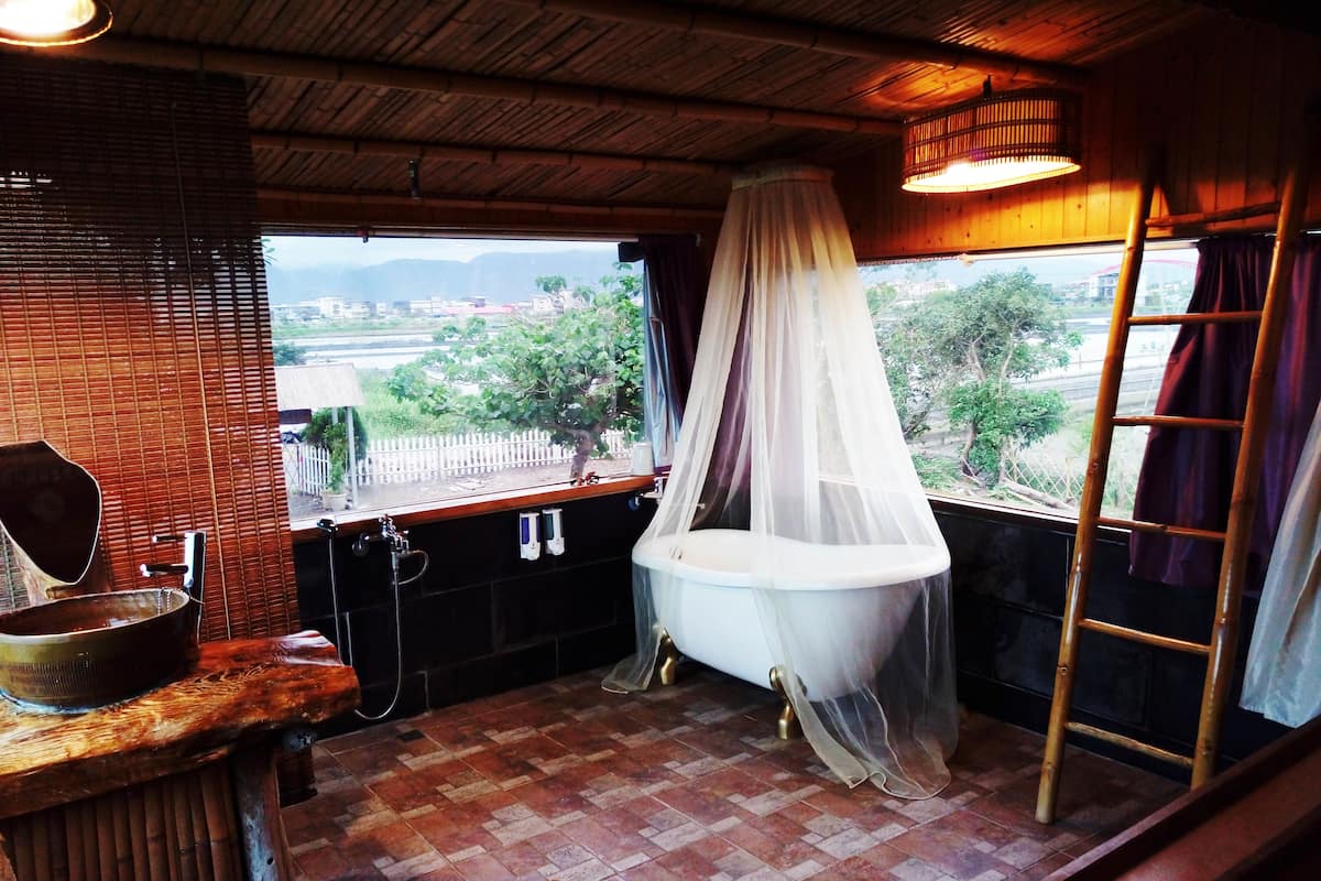 A rustic bathroom with a bathtub under a canopy, a wooden sink, and a view of the outdoors.