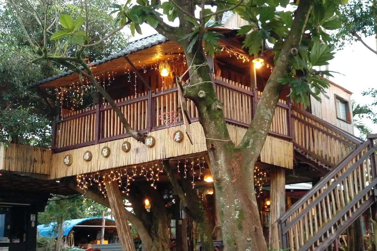 A treehouse with a wooden exterior, a balcony with railings, and string lights.