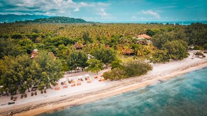 Un complexe hôtelier de bord de mer, avec de nombreuses chaises longues et des parasols, entouré d’une végétation tropicale luxuriante et offrant une vue dégagée sur l’océan.