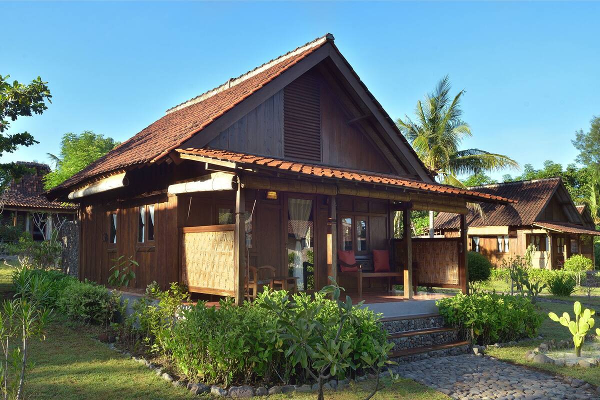 A wooden house with a tiled roof, a porch, and a garden with various plants.