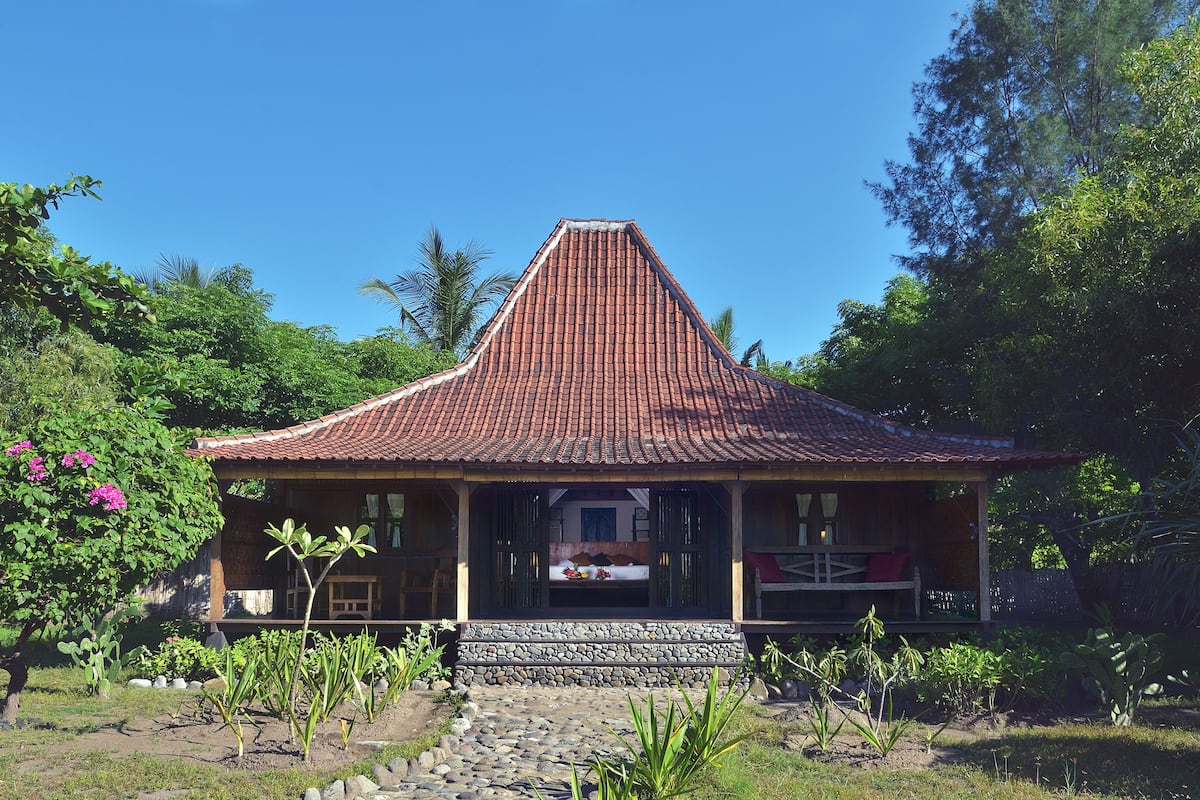 A traditional house with a steeply pitched roof, surrounded by lush greenery and a stone pathway leading to the entrance.