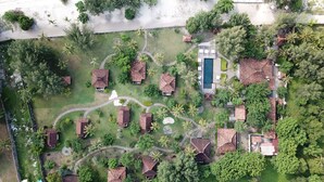 Eine Vogelperspektive zeigt einen Urlaubsort mit mehreren bungalowartigen Gebäuden, einem zentralen Schwimmbad und üppiger, umgebender Vegetation.