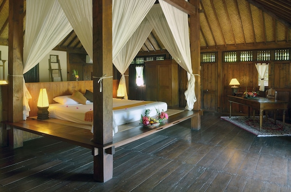 A four-poster bed with a canopy, wooden flooring, a small table with a lamp, and a chair. - Desa Dunia Beda (Gili Trawangan)