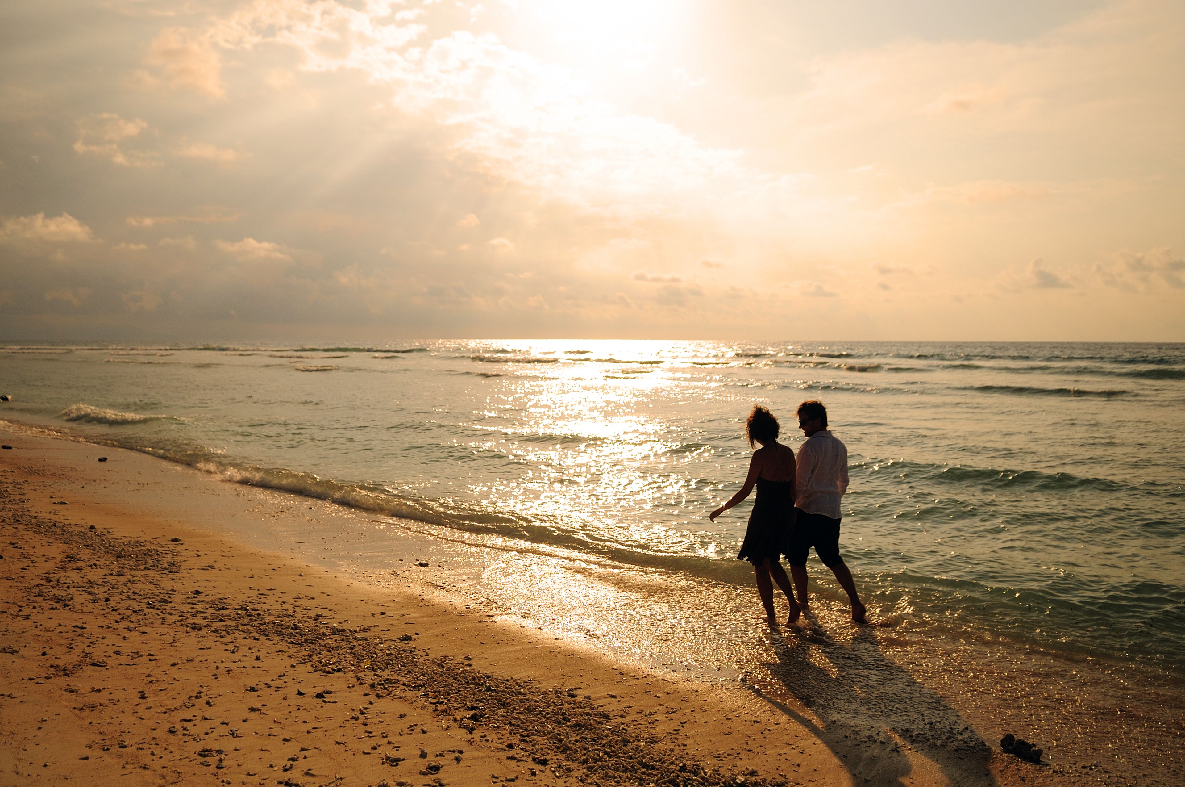 A beach scene with two people walking along the shore.