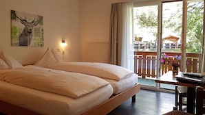 A double bed with white linens, a bedside table with a lamp, and a view of a balcony with flowers. - Parkhotel Saas- Fee (Saas-Fee)