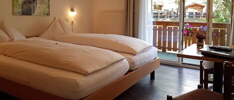 Una cama doble con ropa de cama blanca, una mesita de noche con lámpara y vistas a un balcón con flores.