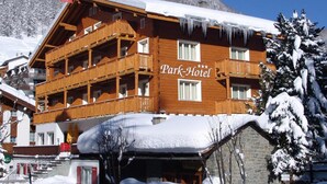 A wooden multi-story building with balconies, labeled "Park-Hotel," surrounded by snow-covered trees and mountains. - Parkhotel Saas- Fee (Saas-Fee)