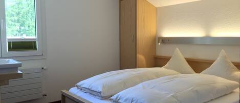 A bedroom with a bed, a nightstand, a window, and a wooden wardrobe.