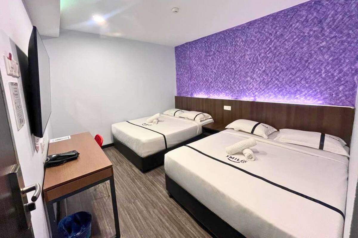 Een hotelkamer met twee bedden, een bureau, een televisie en een paars gestructureerde wand.