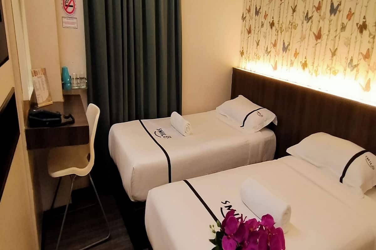 Een hotelkamer met twee bedden, een bureau, een stoel en een raam met gordijnen.