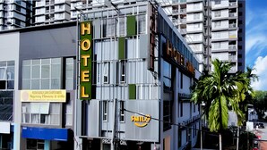 Un hôtel moderne, reconnaissable à son grand panneau lumineux indiquant « HÔTEL », à son logo bien visible représentant un « Sourire » et à l’enseigne « Reseney Fleurs et Cadeaux » située au rez-de-chaussée.