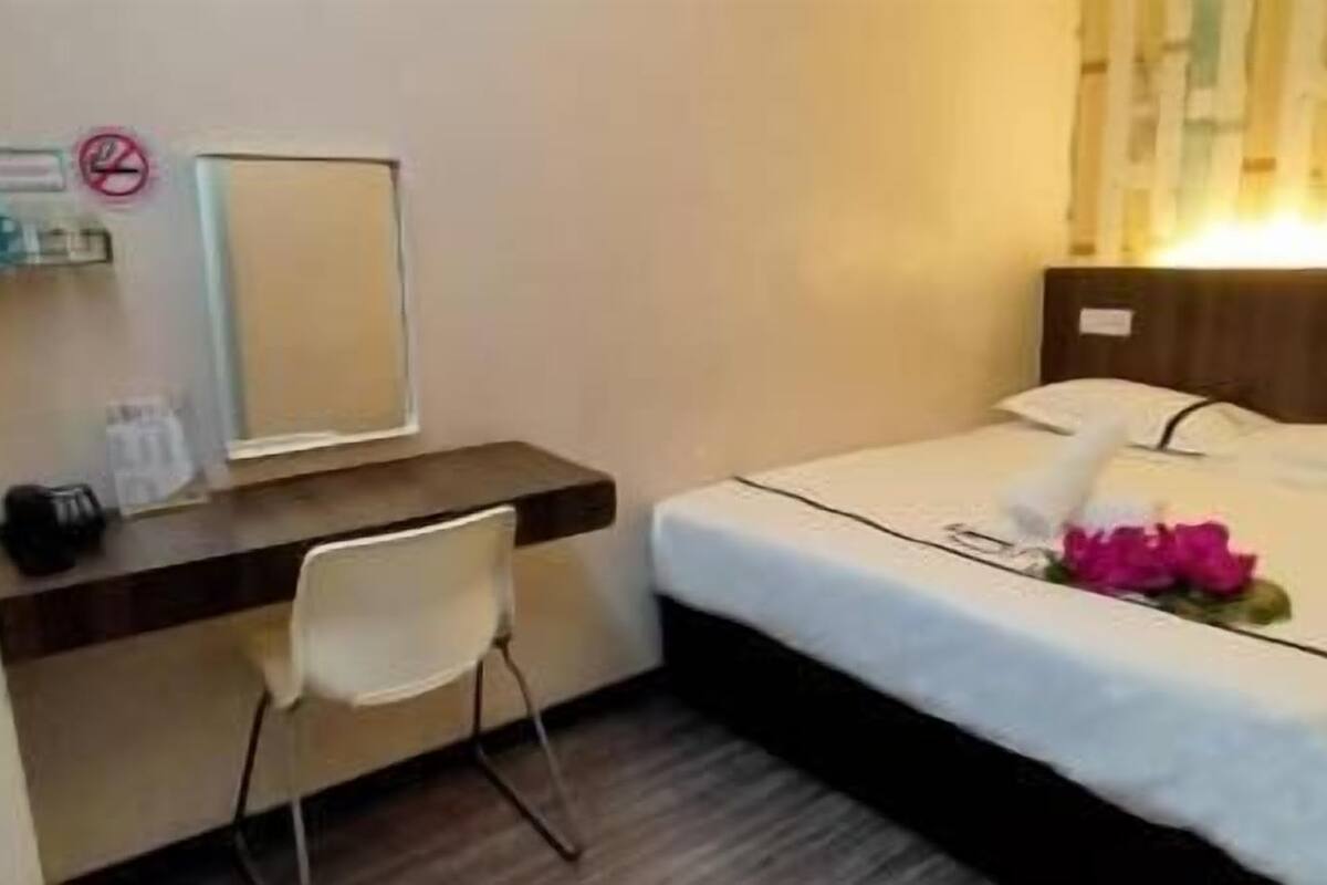 Een hotelkamer met een bed, een bureau, een stoel, een spiegel en een bordje 'niet roken'.
