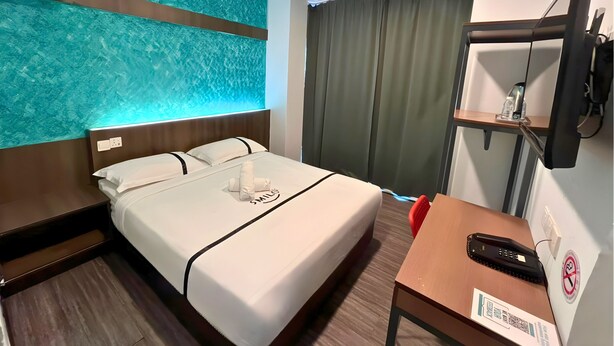 Une chambre d’hôtel équipée d’un lit, d’un bureau, d’un téléphone, d’un téléviseur fixé au mur et d’un rideau.