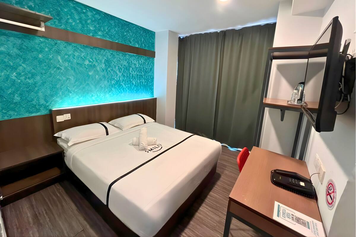 Een hotelkamer met een bed, een bureau, een telefoon, een aan de muur bevestigde televisie en een gordijn.