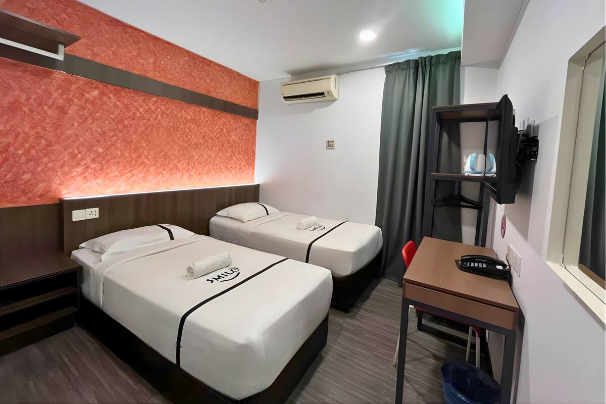 Een hotelkamer met twee bedden, een bureau, een stoel, een airconditioning, een televisie en een wandplank.