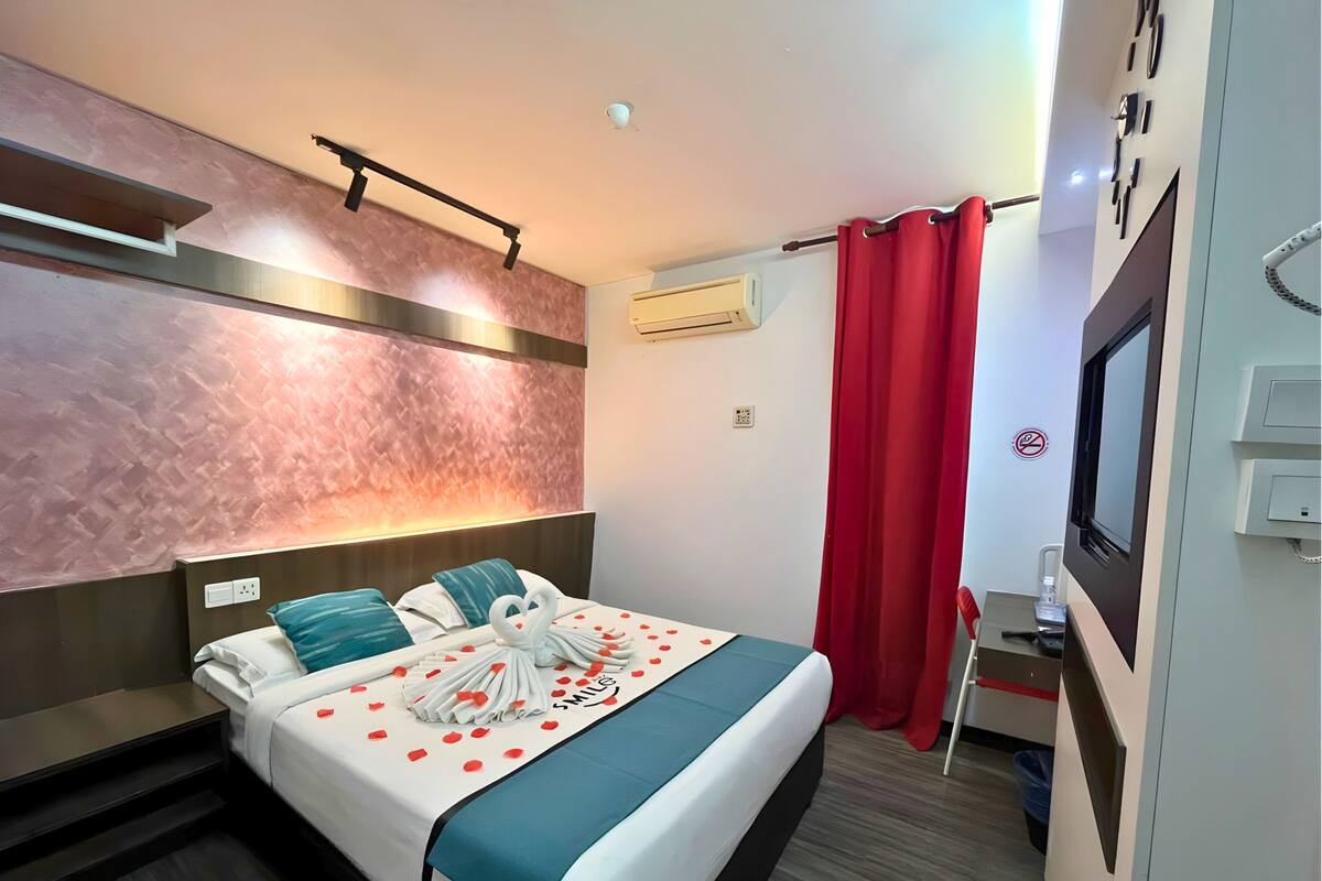 Een hotelkamer met een bed, een televisie, een airconditioning en een rood gordijn.