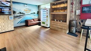 Un hall d’hôtel avec une fresque murale représentant une piscine, un distributeur automatique, un canapé et un comptoir d’accueil.