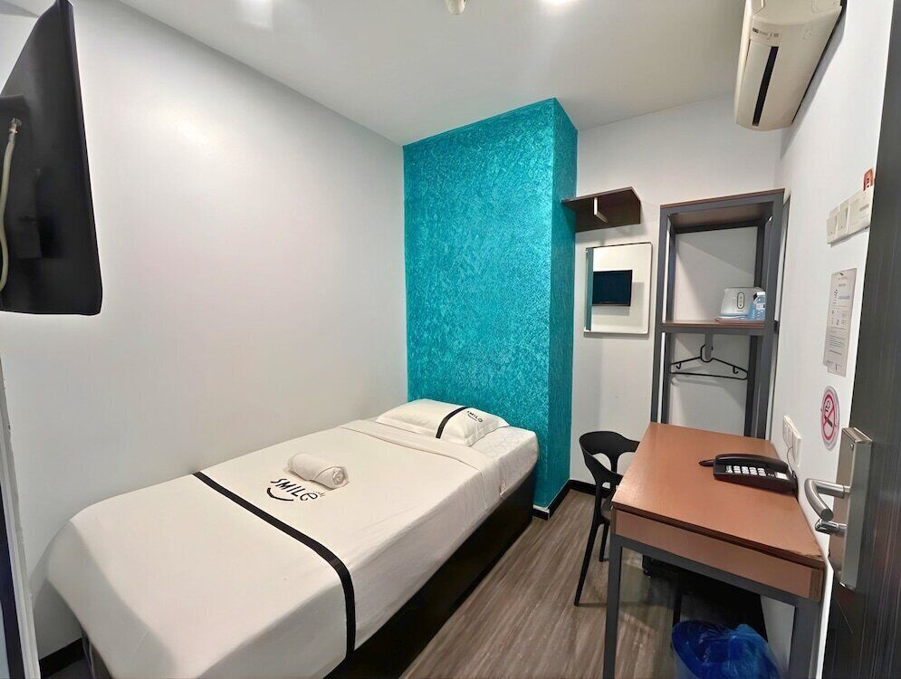 Einzimmer mit einem Bett, einem Schreibtisch, einem Stuhl und einem kleinen Regal mit Spiegel und Telefon.