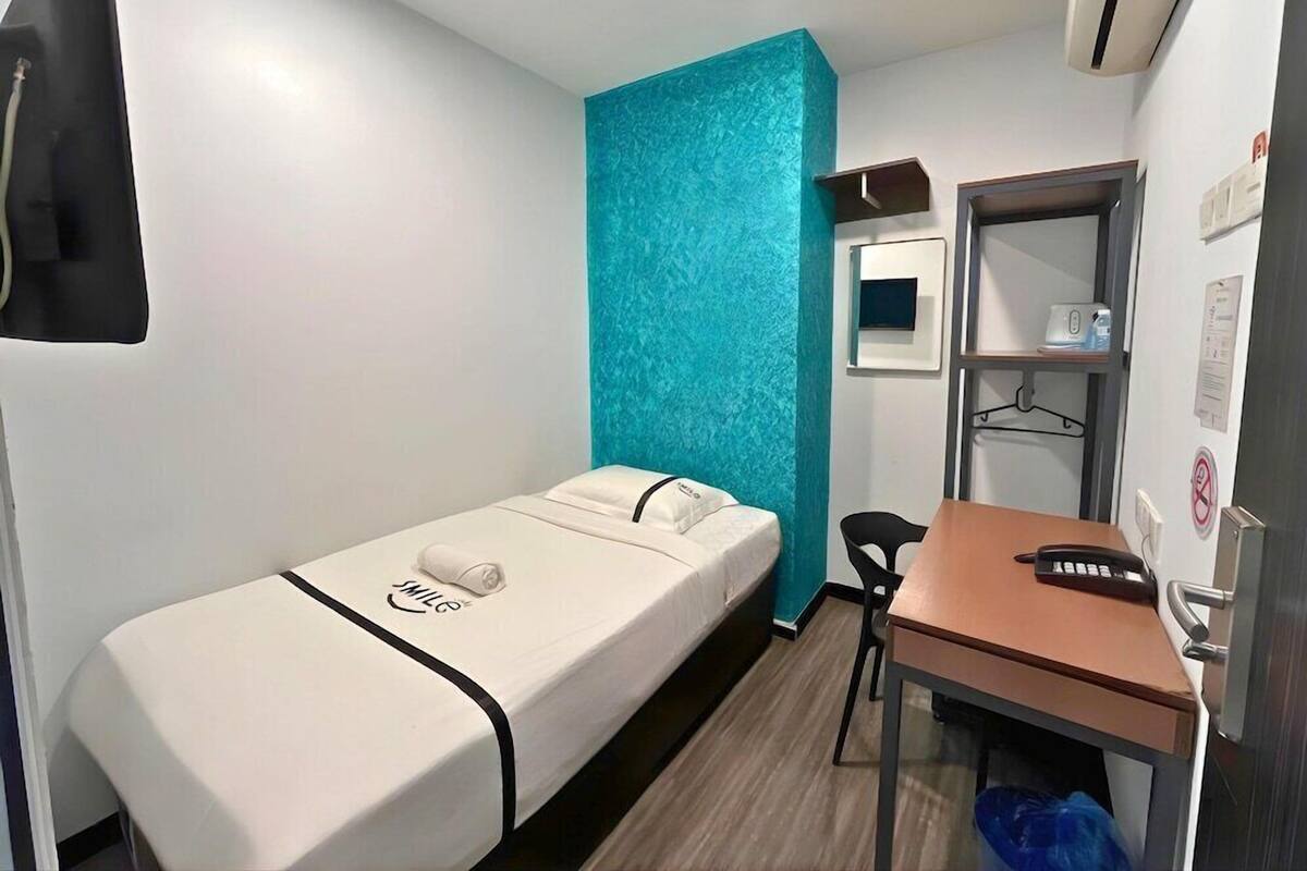 Een kamer met een enkel bed, een bureau, een stoel en een klein plankje met een spiegel en een telefoon.