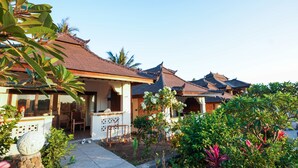 A traditional-style building with a tiled roof, a stone pathway, and lush greenery including palm trees and flowering plants. - Rinjani Lodge (Bayan)