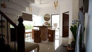 A spacious living area with a wooden staircase, a large clock, and a view of the outdoors. - Pinto Rosario Square Resort and Spa (Guirim)