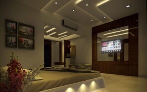 A modern bedroom with a bed, a bedside table, a wall-mounted TV, and a ceiling with recessed lighting. - Rezo's Hotel (Baga)