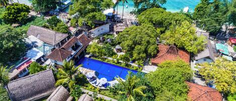 Vista aérea de um resort com piscina, edifícios com telhados de palha e um cais com barcos.