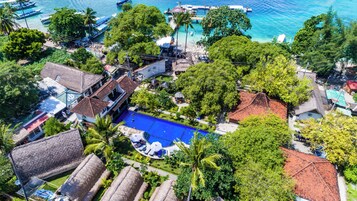 An aerial view of a resort with a swimming pool, thatched-roof buildings, and a dock with boats.