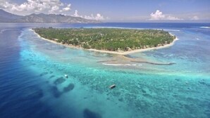 Vue aérienne d’une île tropicale aux eaux turquoise et limpides, avec une petite plage.