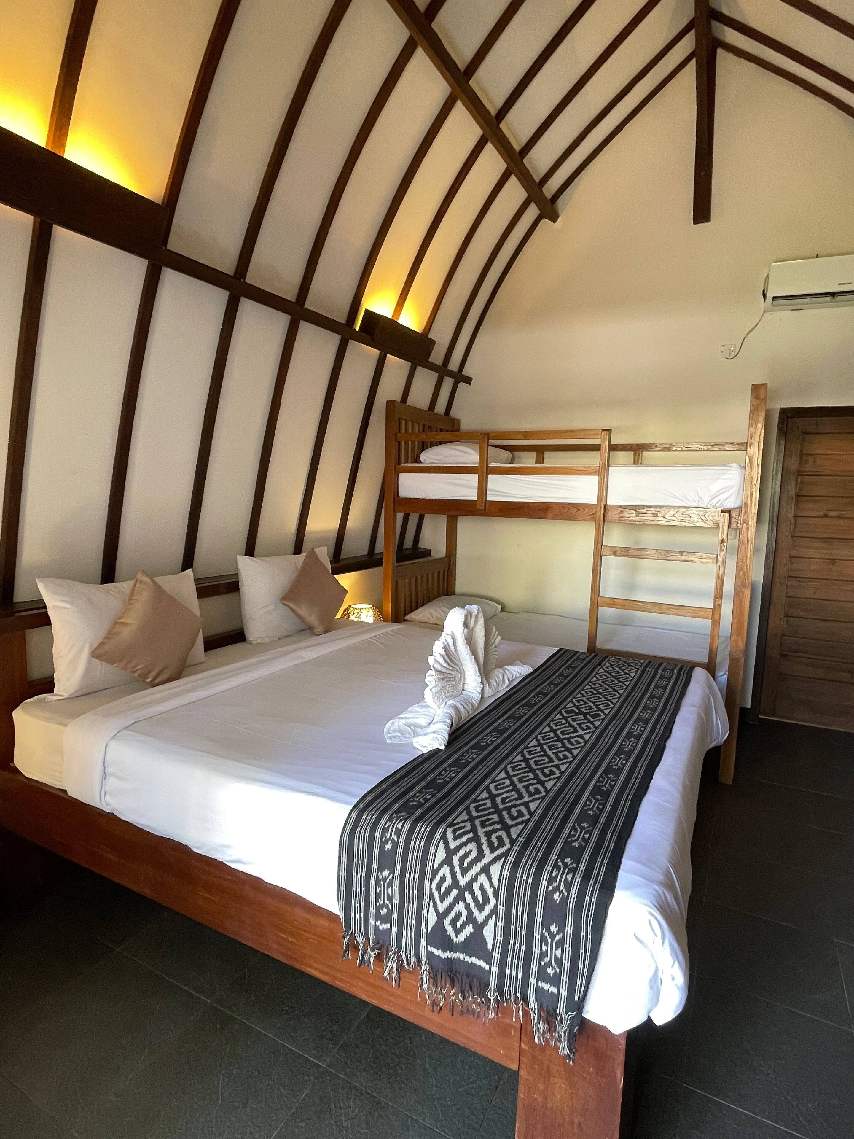 Een kamer met een stapelbed, een groot bed met een bedsprei met dessin, en een houten hoofdbord.
