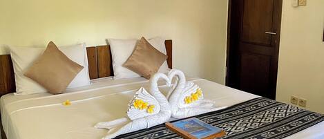 Una cama bien hecha con una colcha estampada, dos toallas con forma de cisne y flores, y un libro sobre la cama.