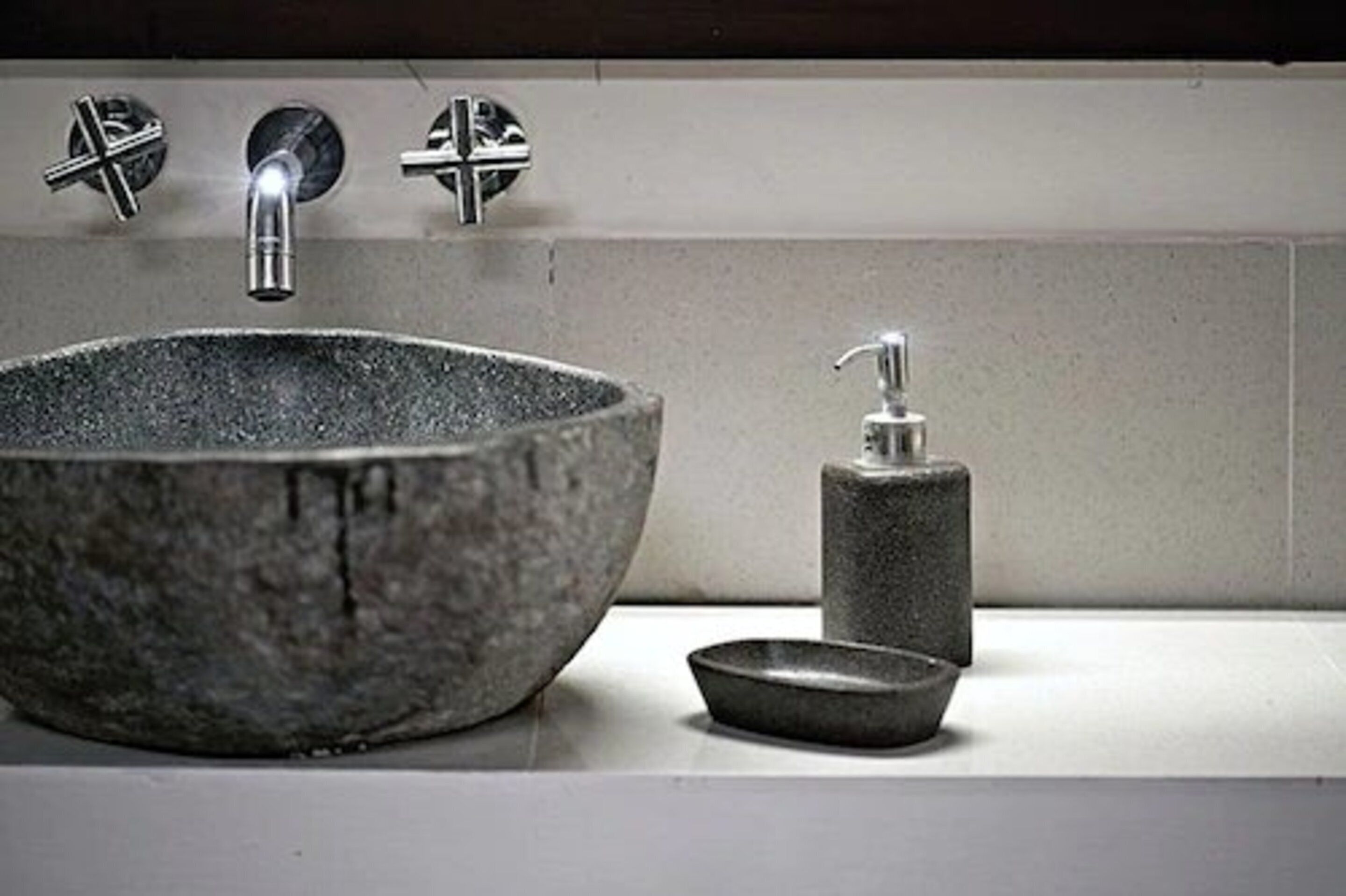 A bathroom with a large stone sink, a faucet, and a soap dispenser.