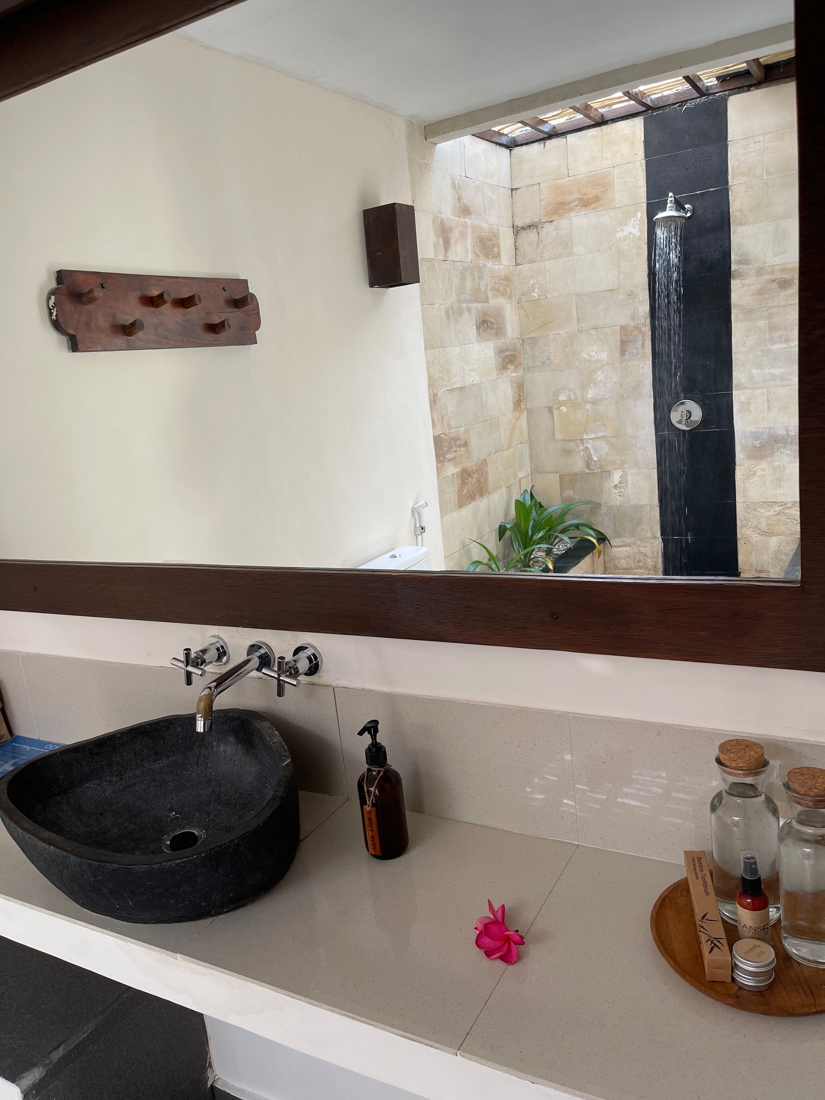 A bathroom with a black sink, a mirror, a shower with a black wall, and a wooden shelf with toiletries.