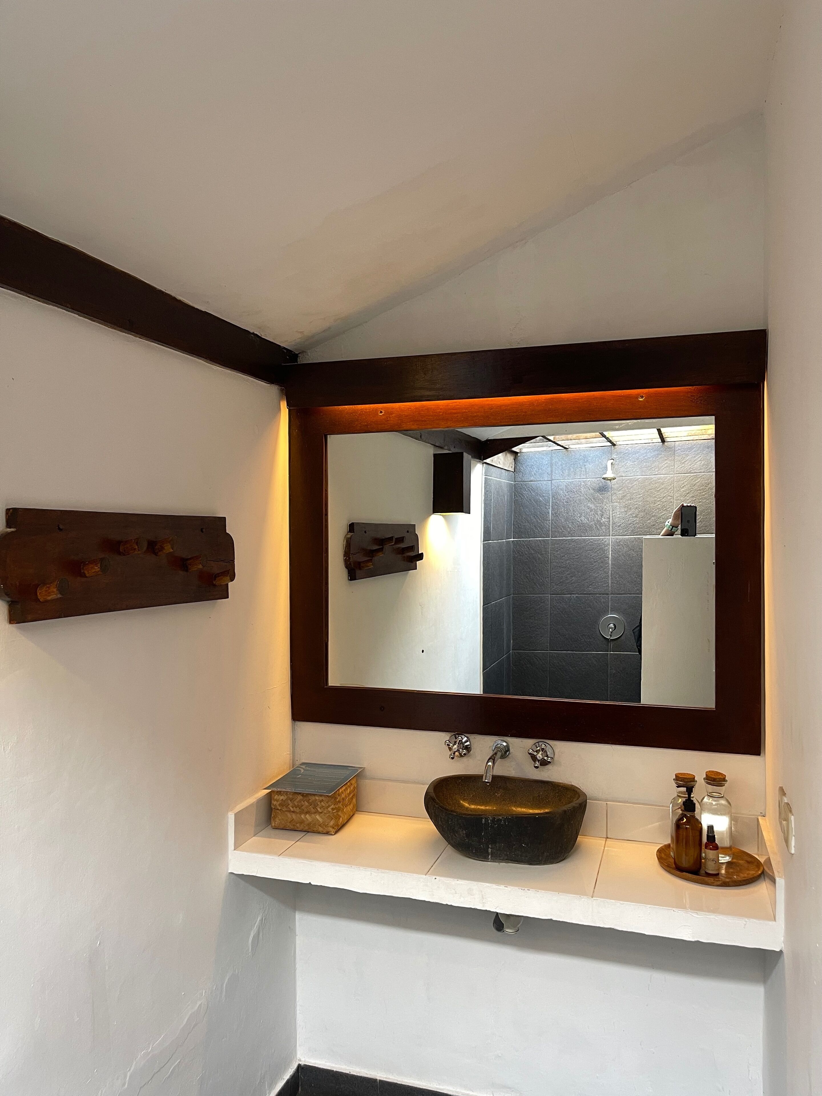 A bathroom with a large mirror, a wooden shelf, a sink with a vessel basin, and a shower area visible in the reflection.