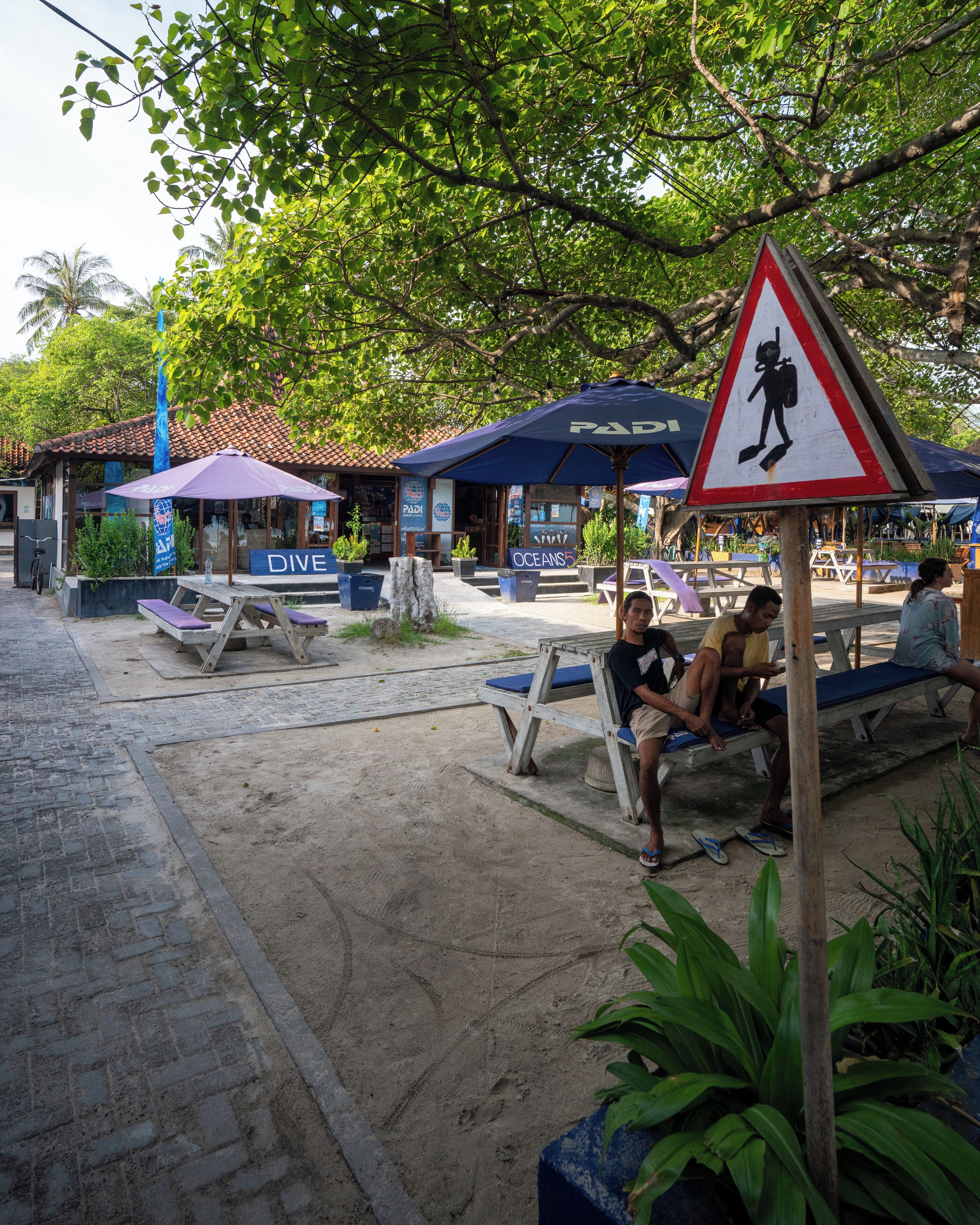 An outdoor seating area with umbrellas, a sign for 'OCEANS5', and a lifeguard warning sign.