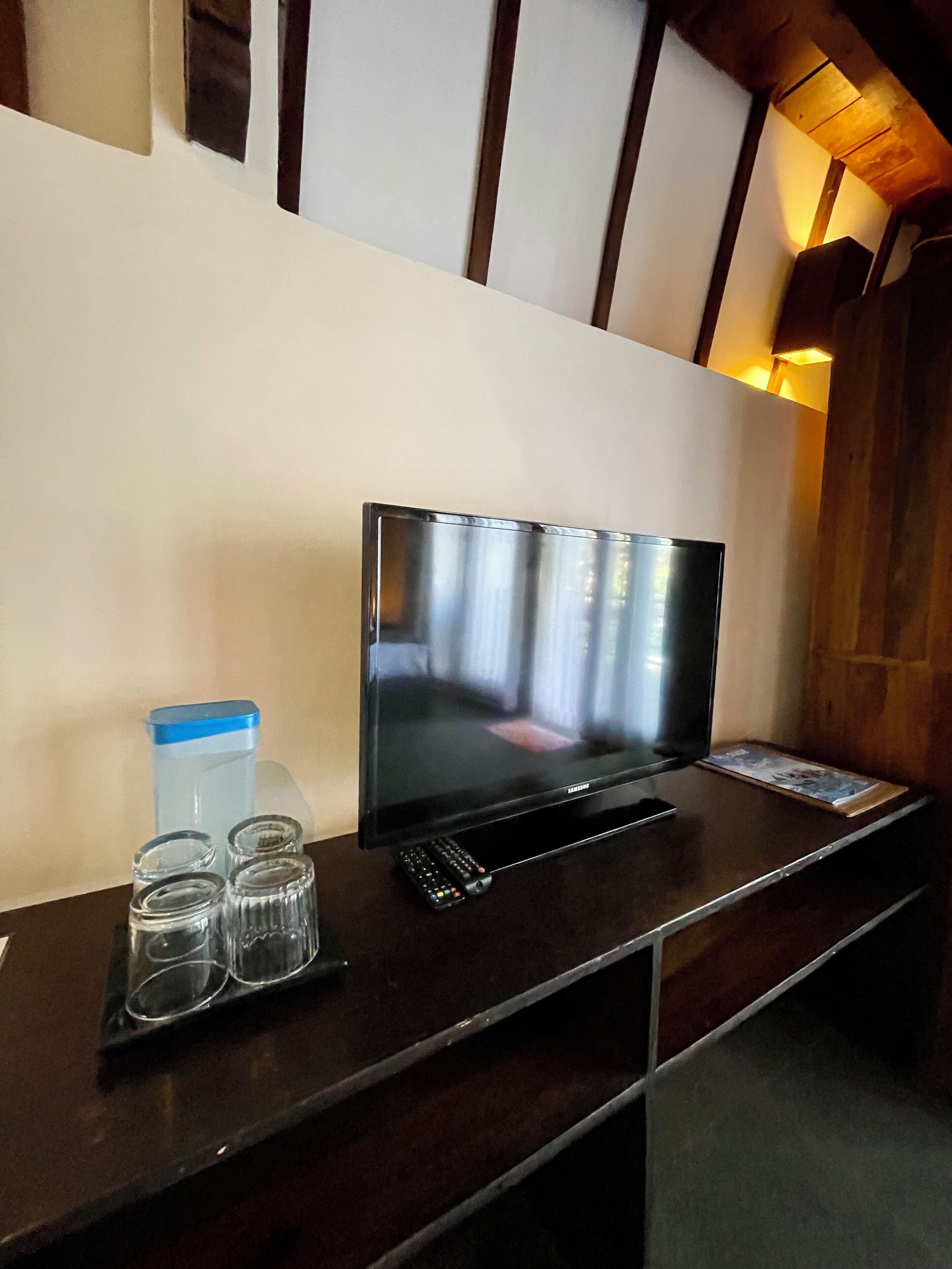 Televisor de pantalla plana sobre un moble de fusta, amb un comandament a distància i quatre vasos.